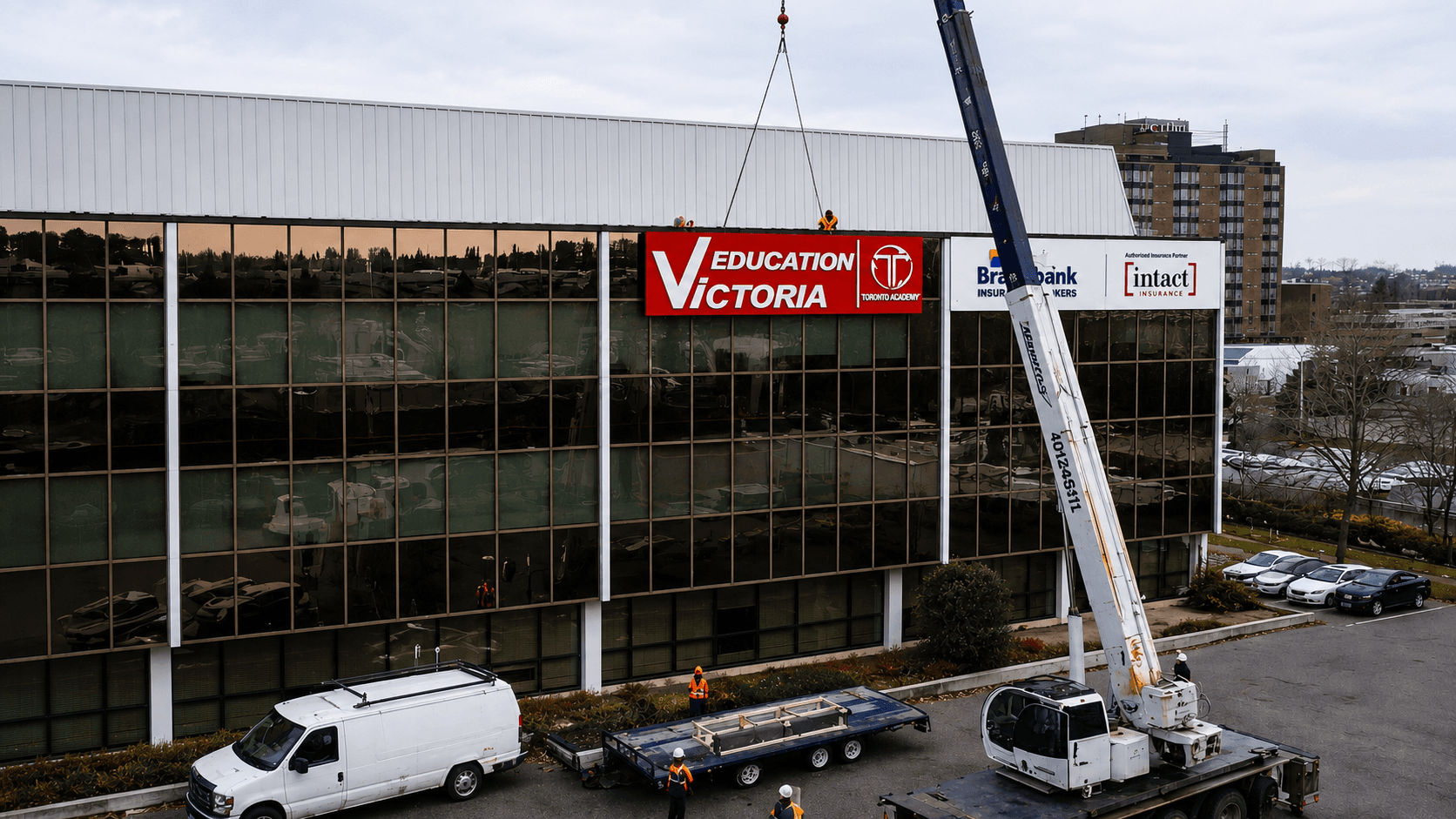 Crane lifting illuminated building signage into place on a commercial office tower