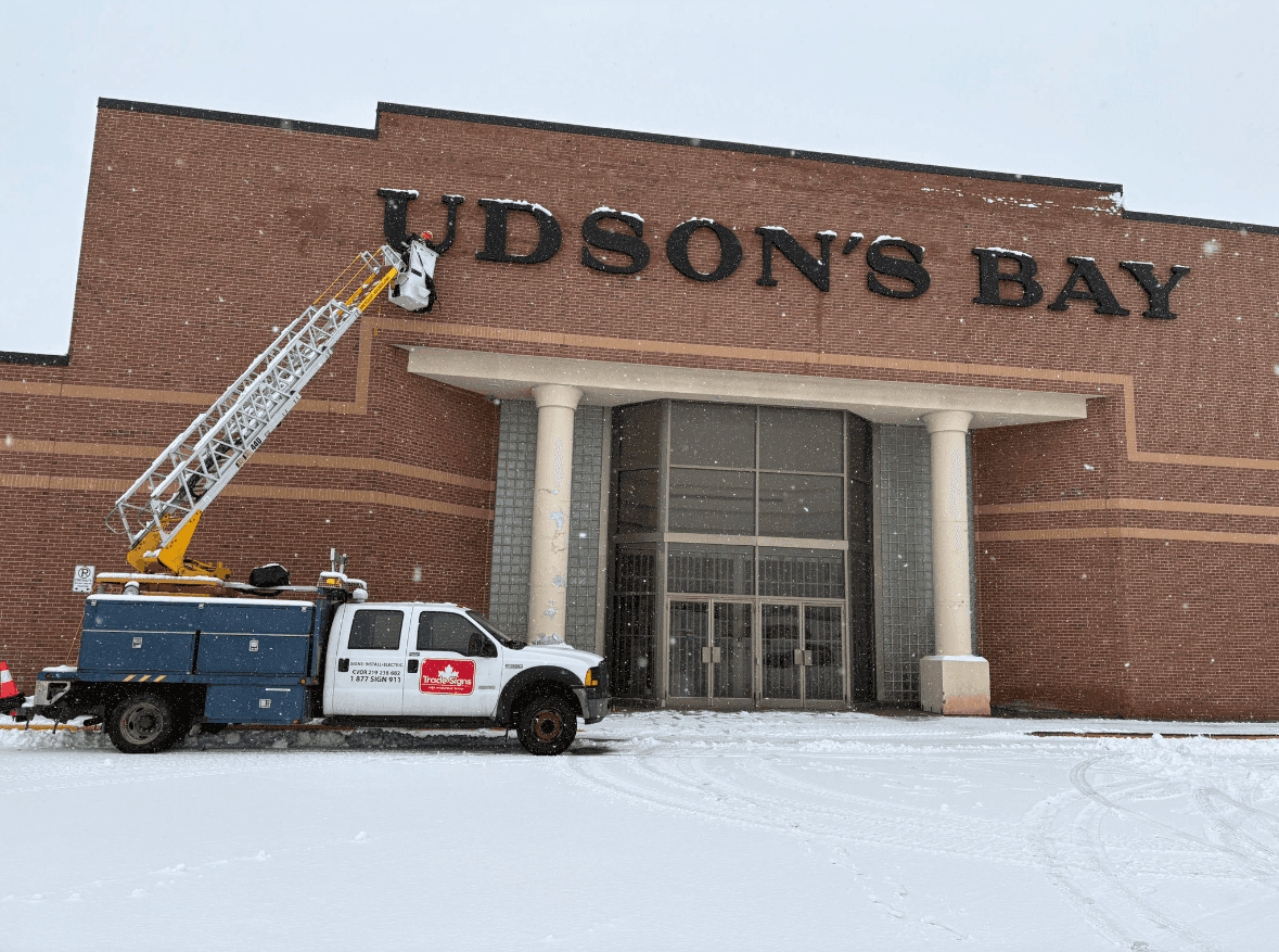 Hudson's Bay sign installation in progress in snow, with letters partially placed