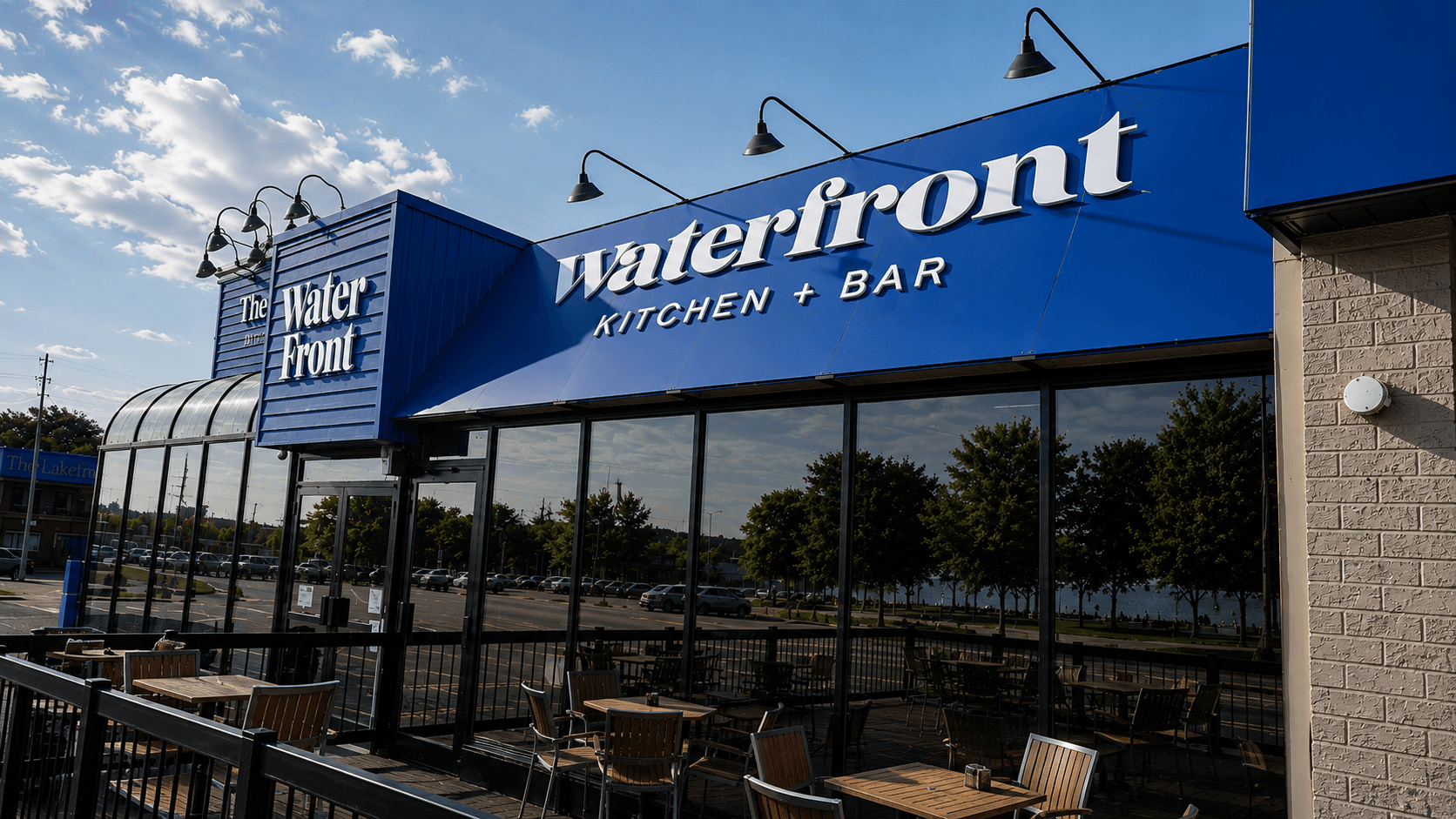 Waterfront Kitchen + Bar illuminated dimensional lettering on a blue metal canopy above a patio